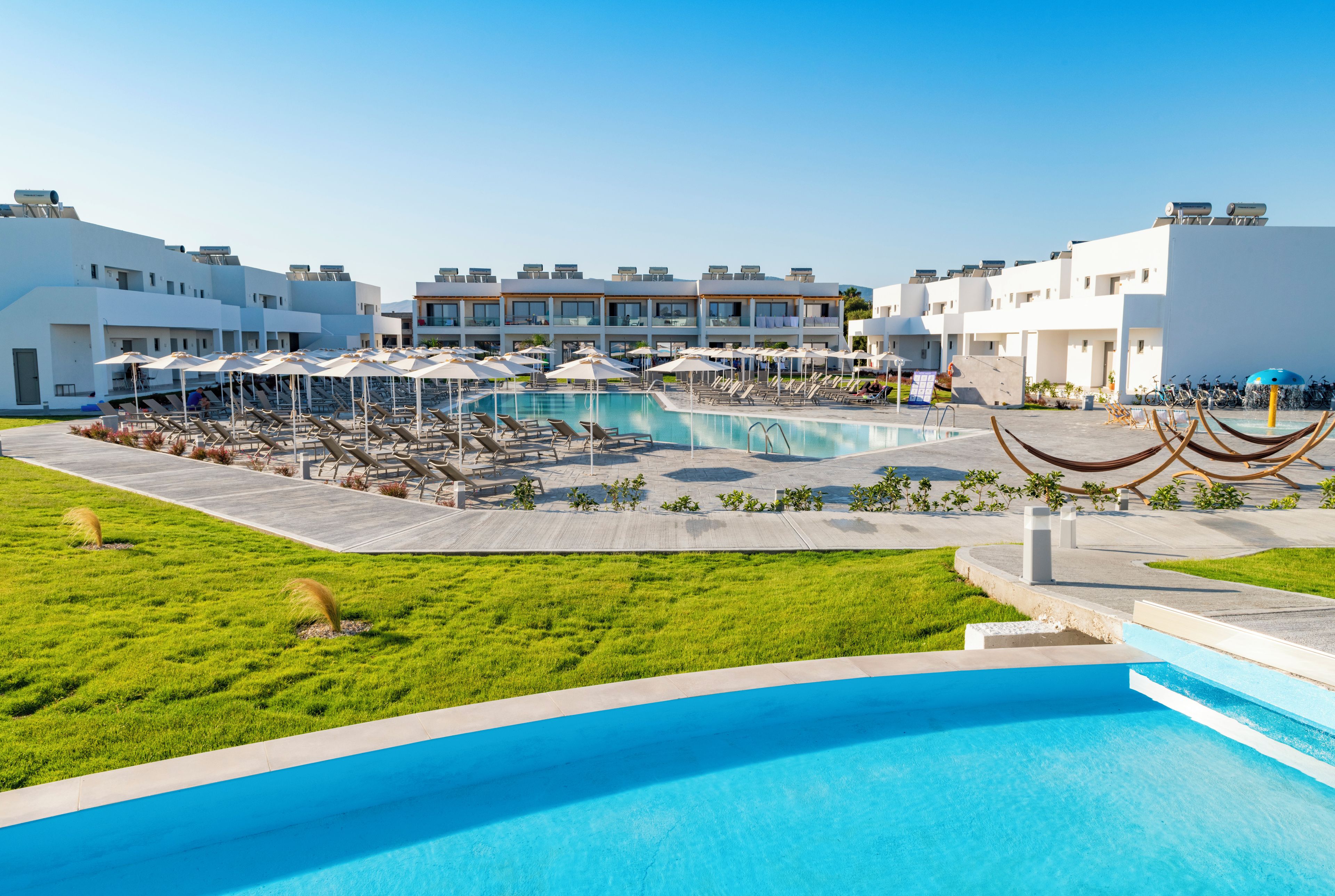 A pool area with lounge chairs and umbrellas, surrounded by modern buildings with balconies.