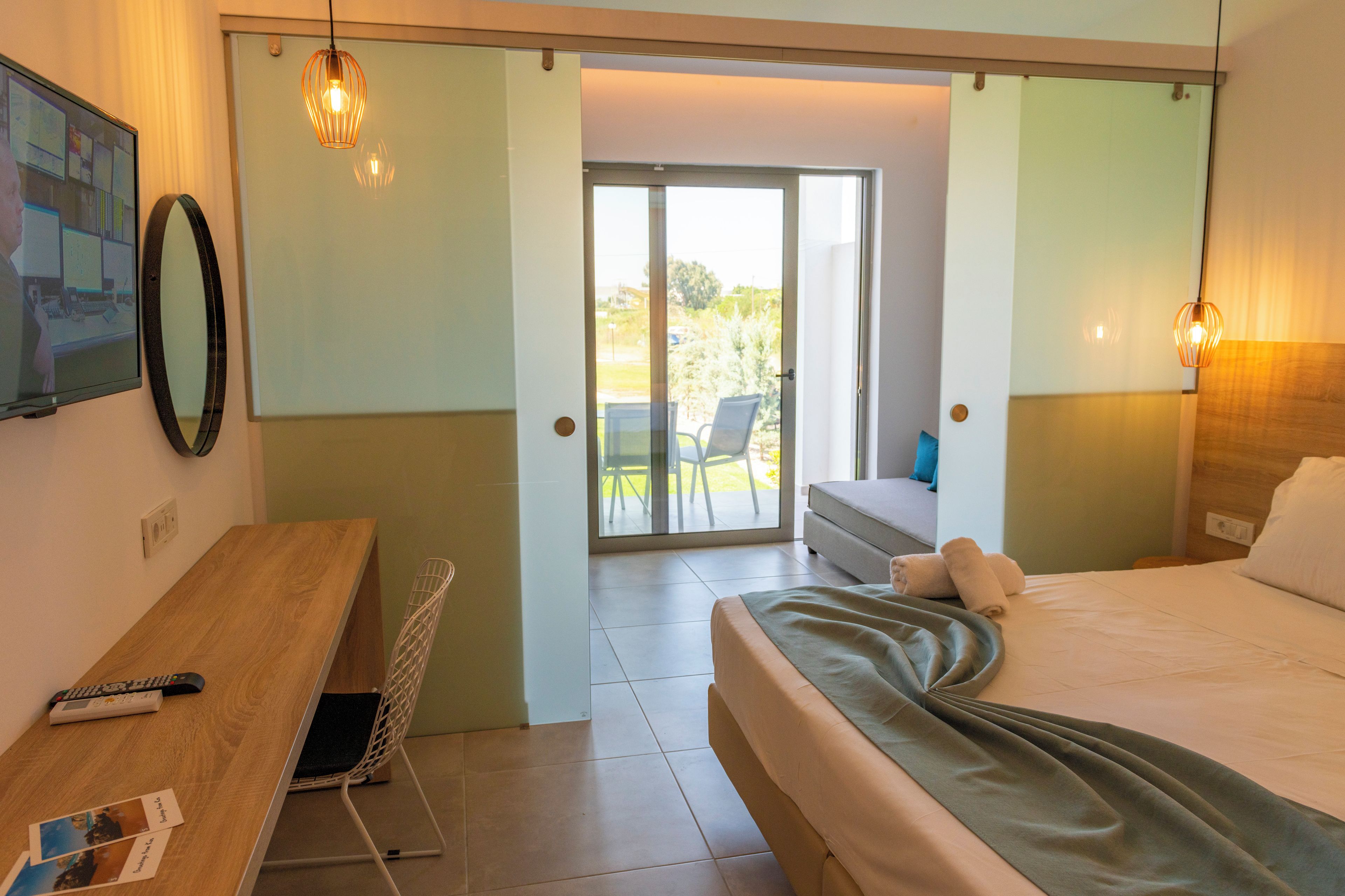 Een hotelkamer met een bed, een bureau, een stoel, een televisie en een balkon met uitzicht op het landschap.