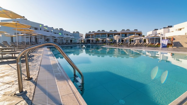 Une piscine dotée de chaises longues et de parasols, entourée de bâtiments modernes.