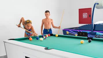 Een biljart met ballen en stokken, een rode brandblusser en een biljarthuiskast.