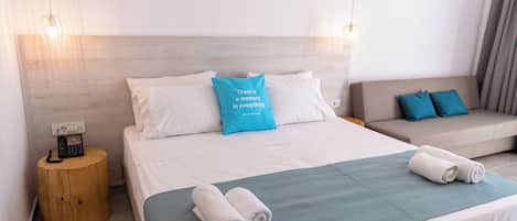 A hotel room with a bed, a bedside table with a phone, a sofa, and a wall-mounted light fixture.