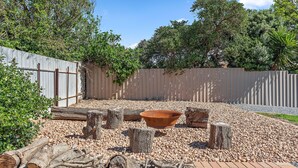 A garden area with a wooden fence, a large terracotta bowl, and scattered logs and stumps.