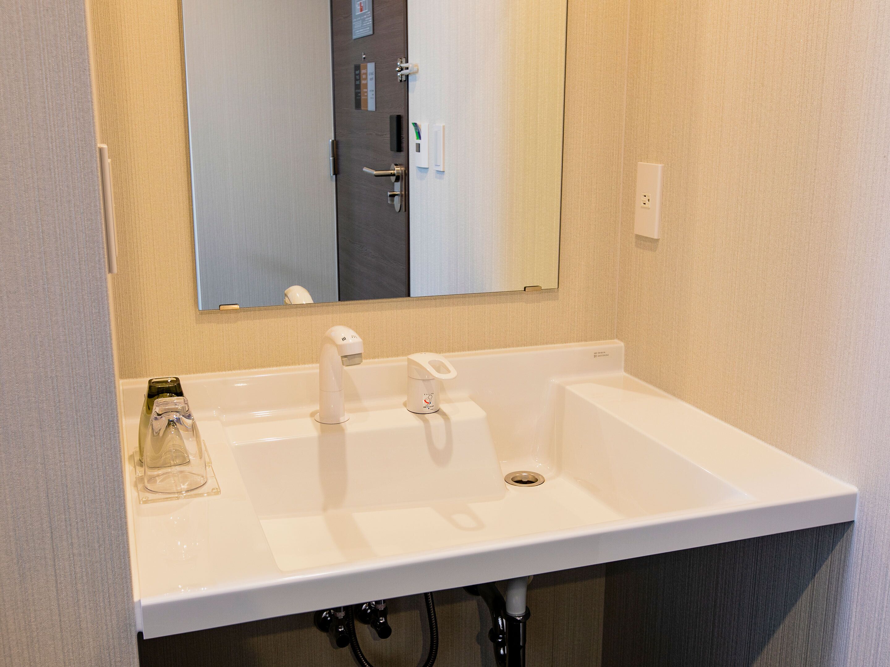 A white bathroom sink with a mirror above it, a towel dispenser, and a soap dispenser.