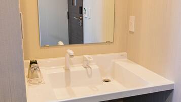 A white bathroom sink with a mirror above it, a towel dispenser, and a soap dispenser.
