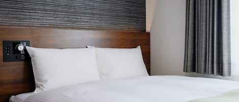 Ein Hotelzimmer mit einem Holzkopfteil, weißer Bettwäsche und einer Bedienkonsole an der Wand.