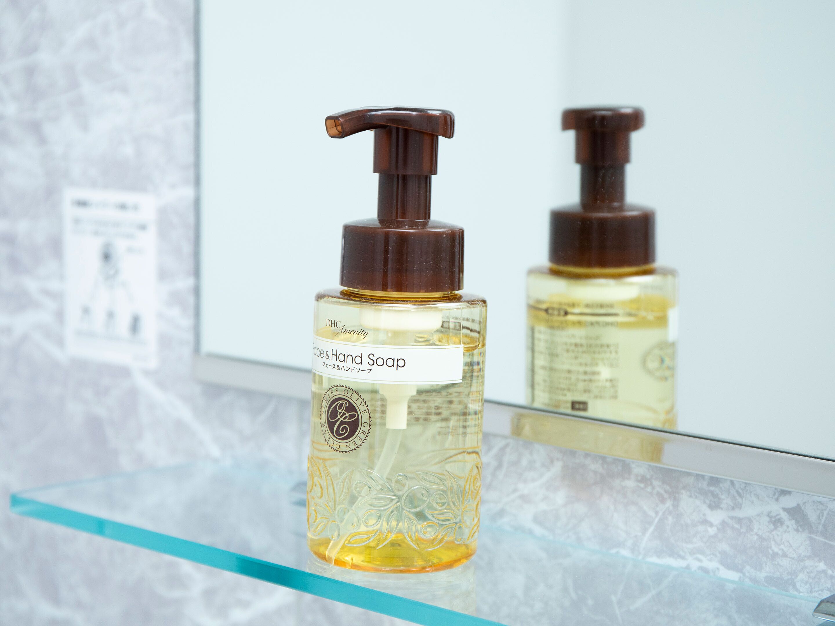 Un baño con un estante de vidrio que sostiene una botella de jabón para manos y rostro.