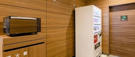 Una kitchenette compacta con microondas, refrigerador y máquina expendedora.