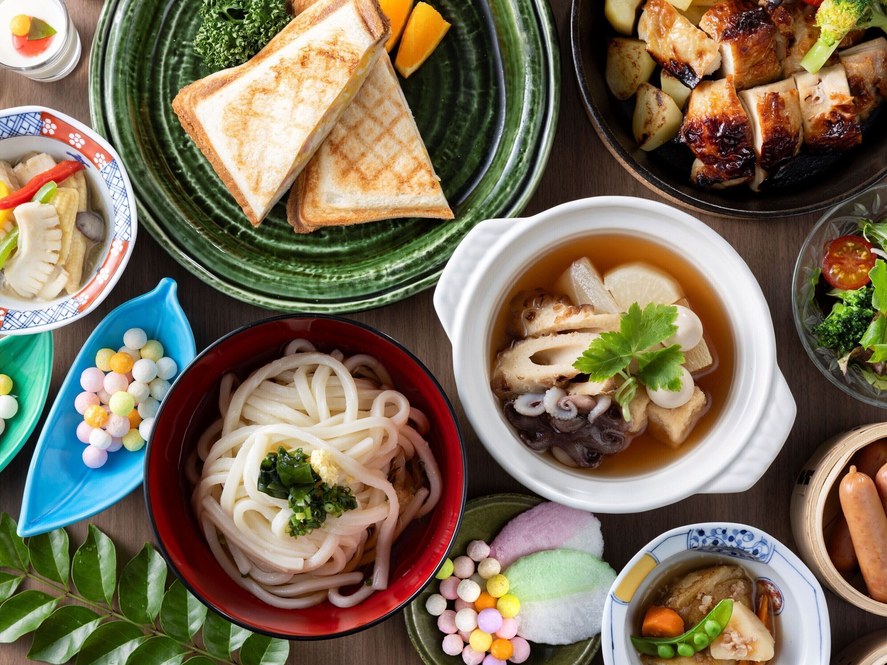 A variety of dishes including noodles, grilled meat, and a bowl of soup.