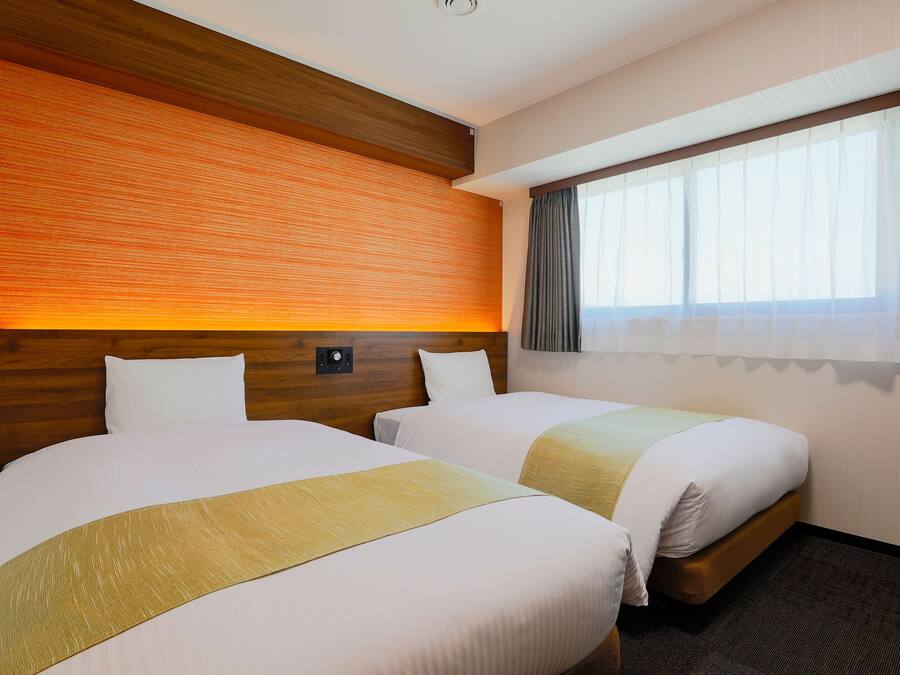 Habitación de hotel con dos camas, cabecero de madera, panel de control y una ventana con cortinas.