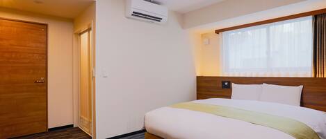 A hotel room with a bed, a wooden headboard, a window with curtains, an air conditioning unit, and a door.