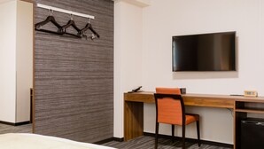 Una habitación de hotel con una cama, un escritorio con una silla, un televisor y un perchero con ganchos.