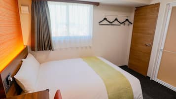 Habitación de hotel con cama, puerta de madera, ventana con cortinas y perchero con ganchos.
