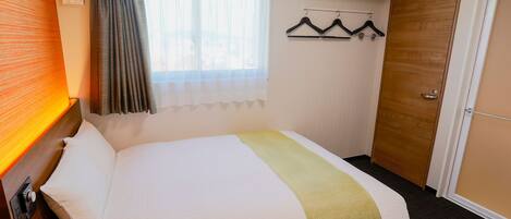 Habitación de hotel con cama, puerta de madera, ventana con cortinas y perchero con ganchos.