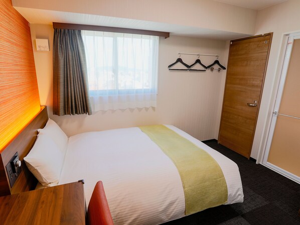 A hotel room with a bed, a wooden door, a window with curtains, and a coat rack with hangers. - KOKO HOTEL Takamatsu (Takamatsu)