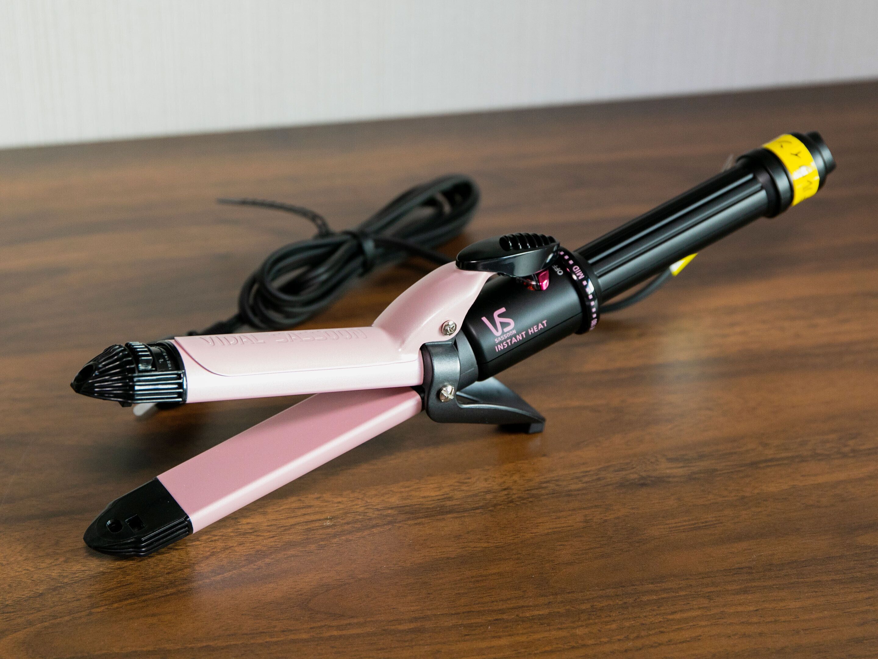 Um alisador de cabelo rosa e preto sobre uma superfície de madeira.