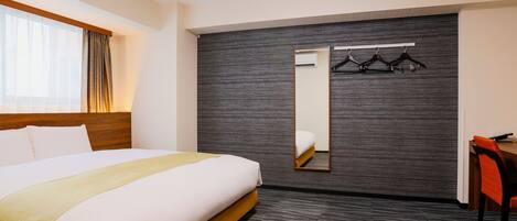 Habitación de hotel con una cama grande, una mesita de noche, una silla, un espejo y un armario con perchas.