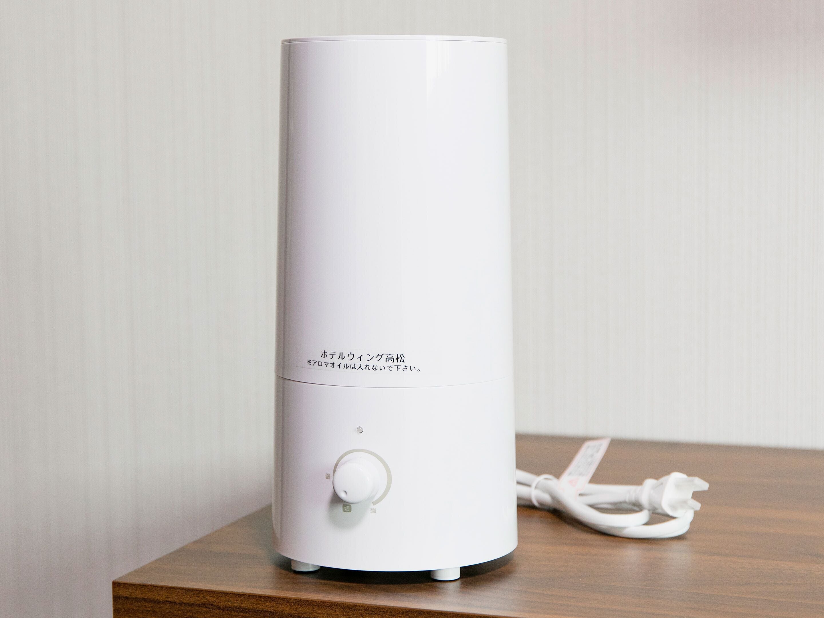 Un appareil cylindrique blanc, doté d’un bouton de commande et d’un câble d’alimentation, posé sur une surface en bois.