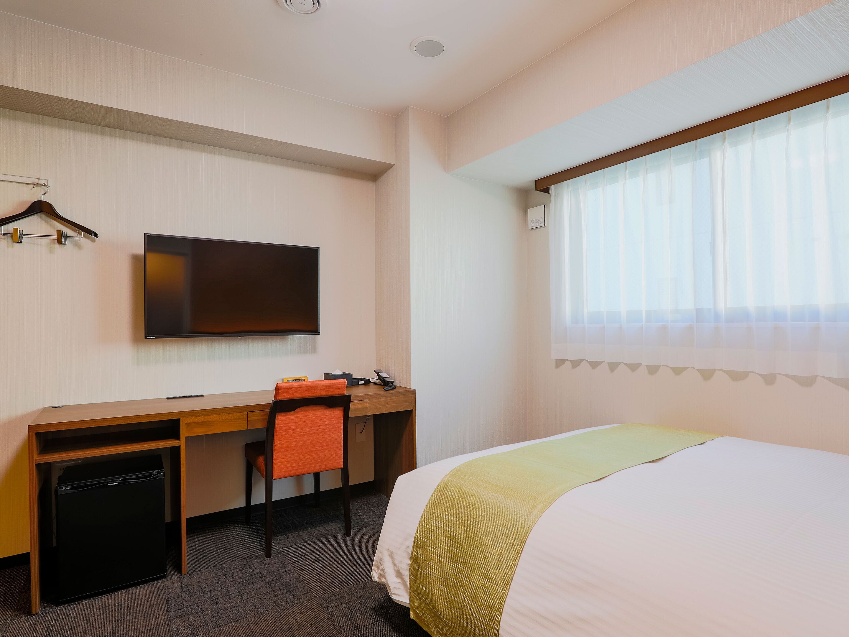 Una habitación de hotel con cama, escritorio con silla, televisor y ventana con cortinas.