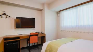 Habitació d'hotel amb llit, escriptori i cadira, televisió i finestra amb cortines.