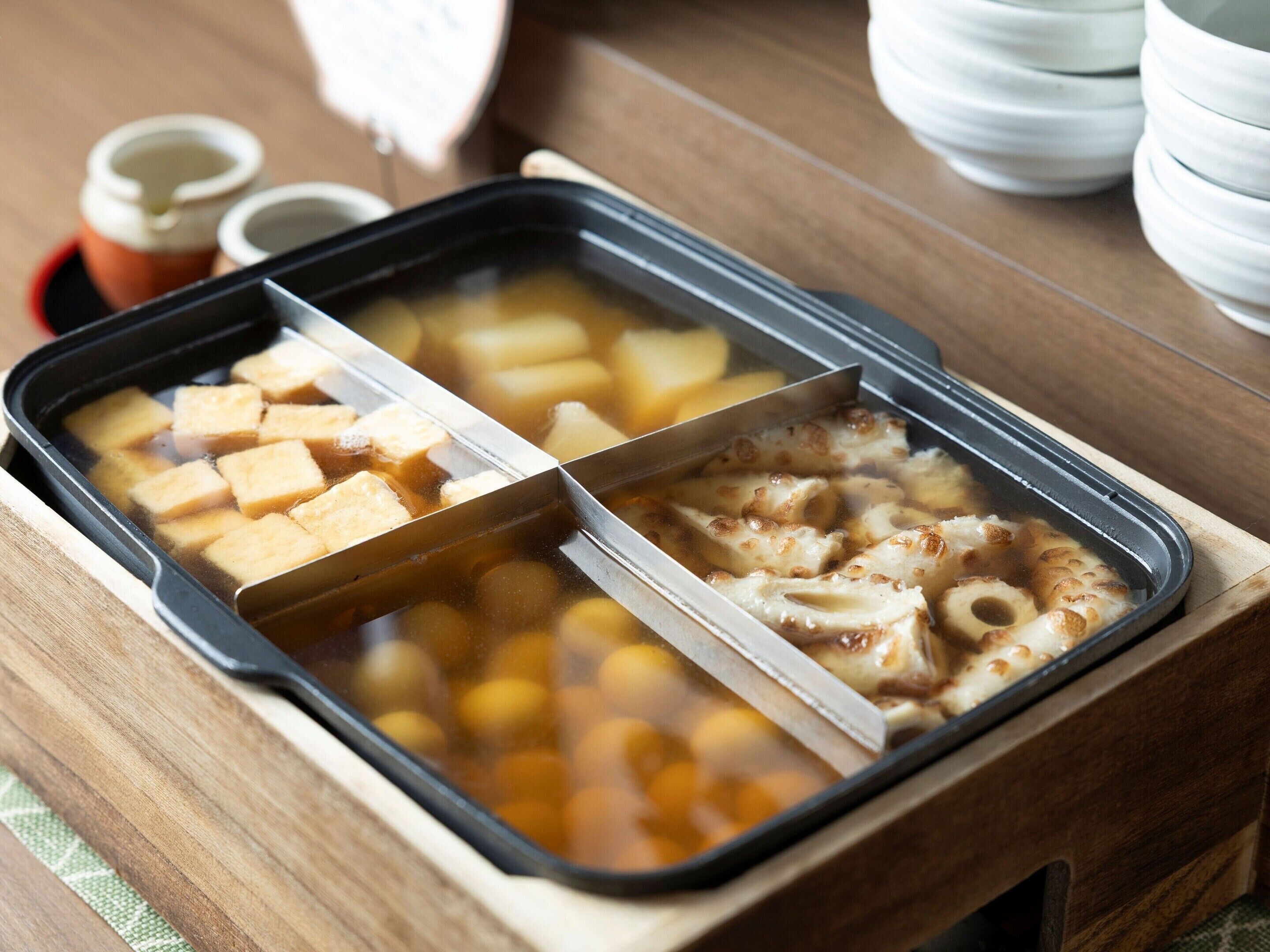Una olla caliente con tofu, champiñones y otras verduras en una bandeja de madera.