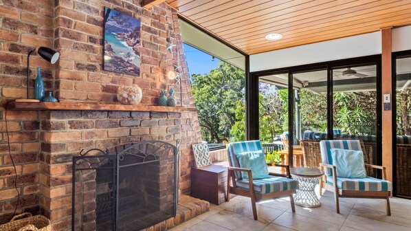 A brick fireplace with a glass door, a blue vase, and a framed picture on the mantel. There are wicker chairs and a small round table in the foreground.