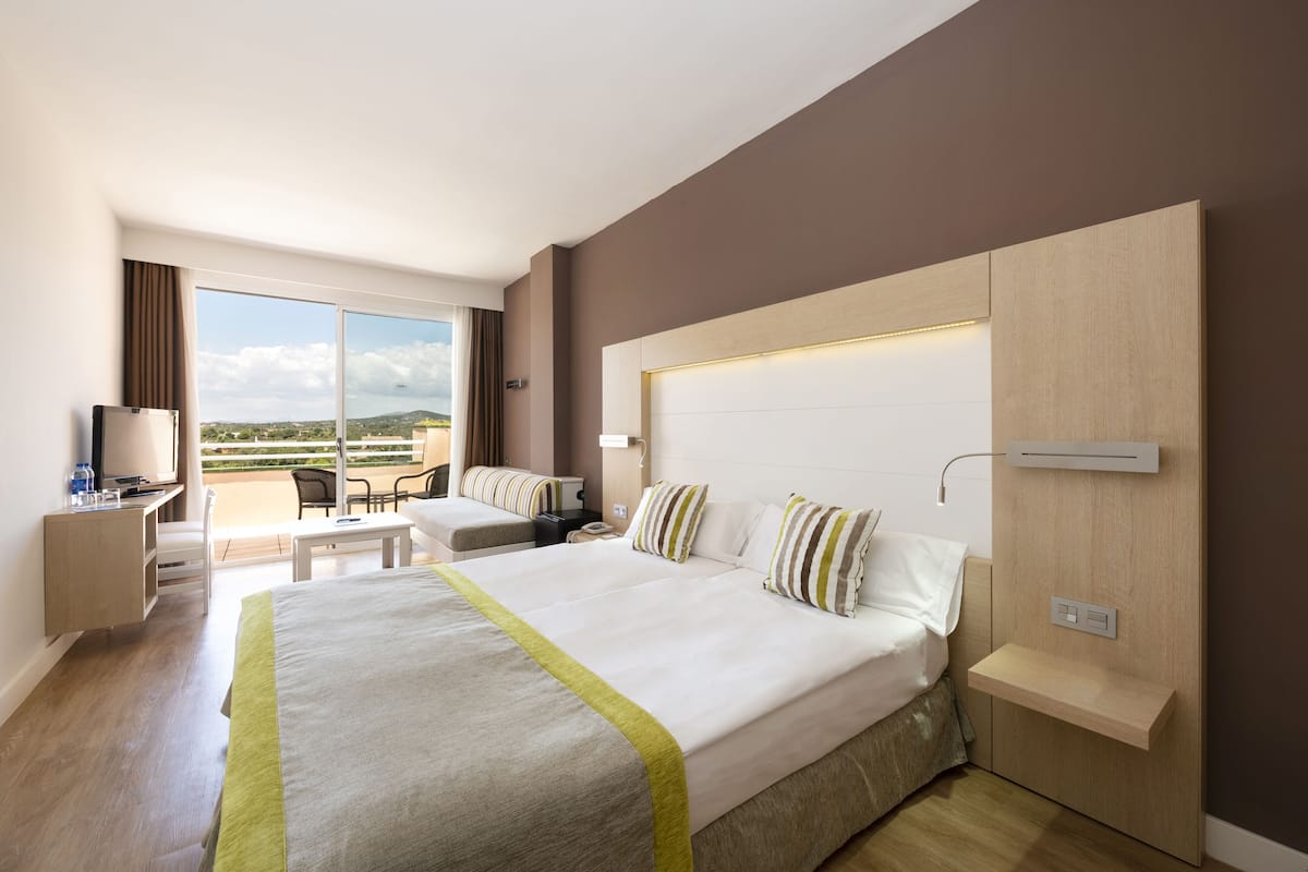 A hotel room with a large bed, a desk, a chair, and a balcony with a view.