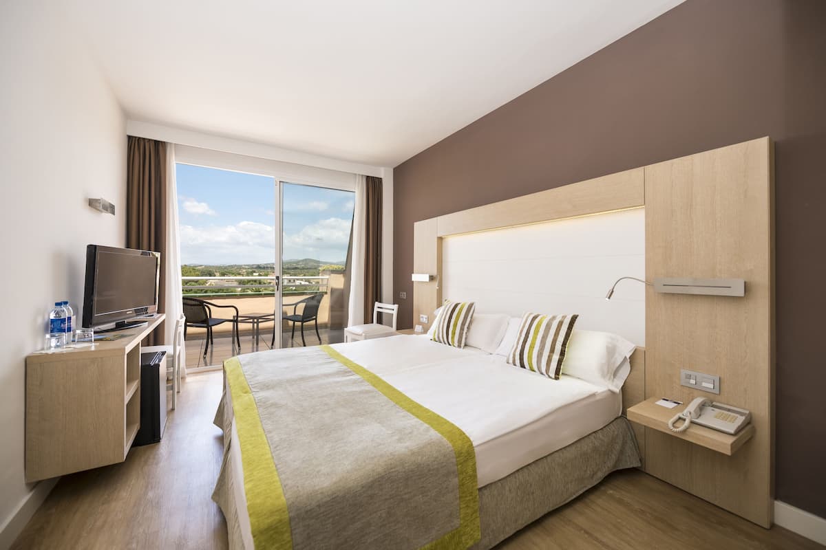 A hotel room with a large bed, a desk with a TV, a phone, and a view of the outdoors.