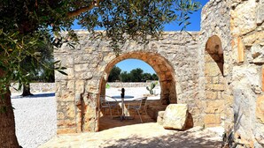 An ancient stone archway leading to a courtyard with a table and chairs, surrounded by olive trees and a cactus. - Modern trulli, 3 bedrooms, air conditioning, private swimming pool, pétanque court. (Castellana Grotte)