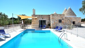 A swimming pool with lounge chairs and a stone building with conical roofs. - Modern trulli, 3 bedrooms, air conditioning, private swimming pool, pétanque court. (Castellana Grotte)