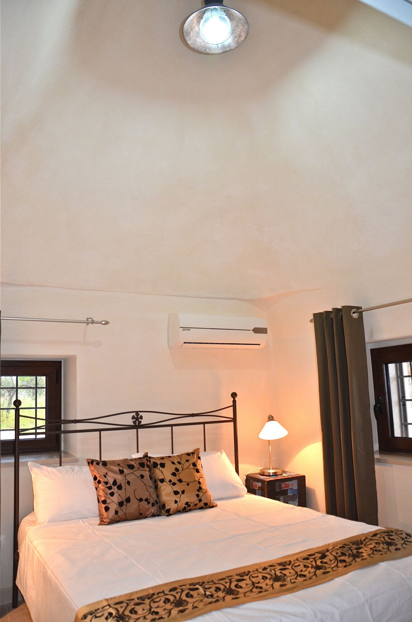 Une chambre à coucher comprenant un lit, une table de chevet avec une lampe, un appareil de climatisation et une fenêtre avec des rideaux.