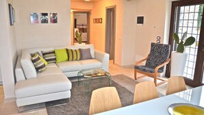 A living room with a white sofa, a glass coffee table, and a patterned armchair. There is a dining table with chairs and a cactus plant. - Modern trulli, 3 bedrooms, air conditioning, private swimming pool, pétanque court. (Castellana Grotte)