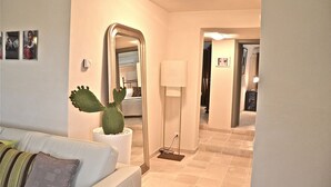 A hotel room with a white sofa, a cactus plant, a floor lamp, and a mirror reflecting a bed and an air conditioning unit. - Modern trulli, 3 bedrooms, air conditioning, private swimming pool, pétanque court. (Castellana Grotte)