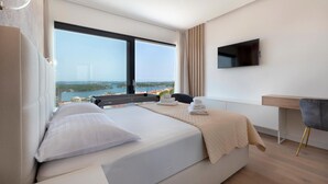 Ein modernes Hotelzimmer mit einem großen Bett, einem Schreibtisch, einem Sessel, einem Fernseher und Meerblick.