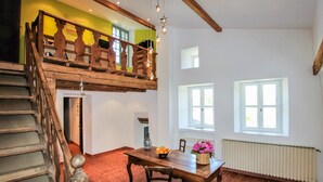 Un'area pranzo con un tavolo e sedie in legno, una scala con ringhiera in legno e vista sull'esterno attraverso le finestre.