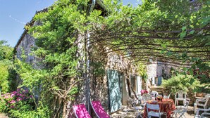 Zona esterna con tavoli e sedie, circondata da vegetazione e un edificio in pietra.