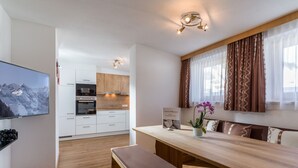 A modern kitchen with white cabinets, a wooden countertop, and a built-in oven. There is a dining area with a bench and a table, and a TV mounted on the wall. - Apartment mit 3 Schlafzimmern und Balkon (Gerlos)