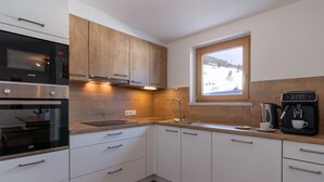A modern kitchen with white cabinets, a built-in oven, a coffee maker, and a window with a view of a snowy landscape. - Apartment mit 3 Schlafzimmern und Balkon (Gerlos)