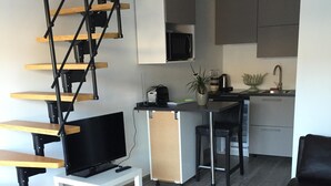 Ett modernt vardagsrum med en trätrappa, en platt-TV, ett litet vitt bord och en svart lädersoffa.