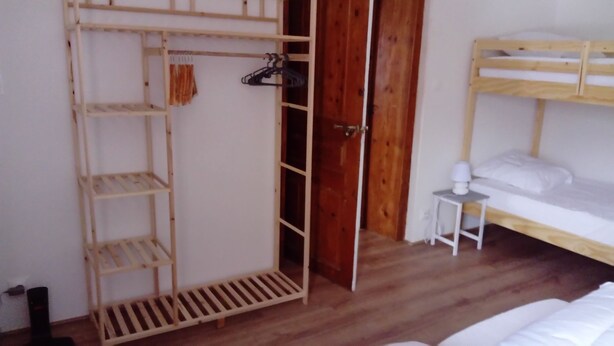 A room with a wooden bunk bed, a small bedside table with a lamp, and a wooden wardrobe with shelves and hanging space.