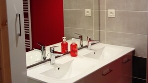 A modern bathroom with two sinks, a mirror, and a red accent wall.