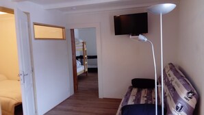 A narrow hallway with a bunk bed in the background, a television mounted on the wall, and a floor lamp.