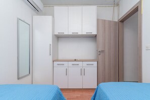 A bedroom with two single beds, a wardrobe, and a small kitchenette.