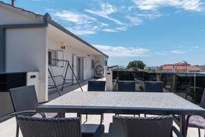 An outdoor patio with a table and chairs, a hanging chair, and a view of the sea.