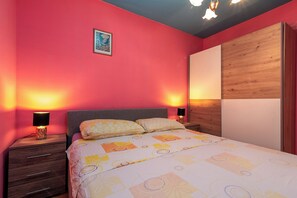 A bedroom with a bed, two bedside tables, a nightstand, a wooden wardrobe, and a framed picture on the wall.