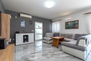 A modern living room with a sofa, a coffee table, and a kitchen area with a refrigerator and a microwave.