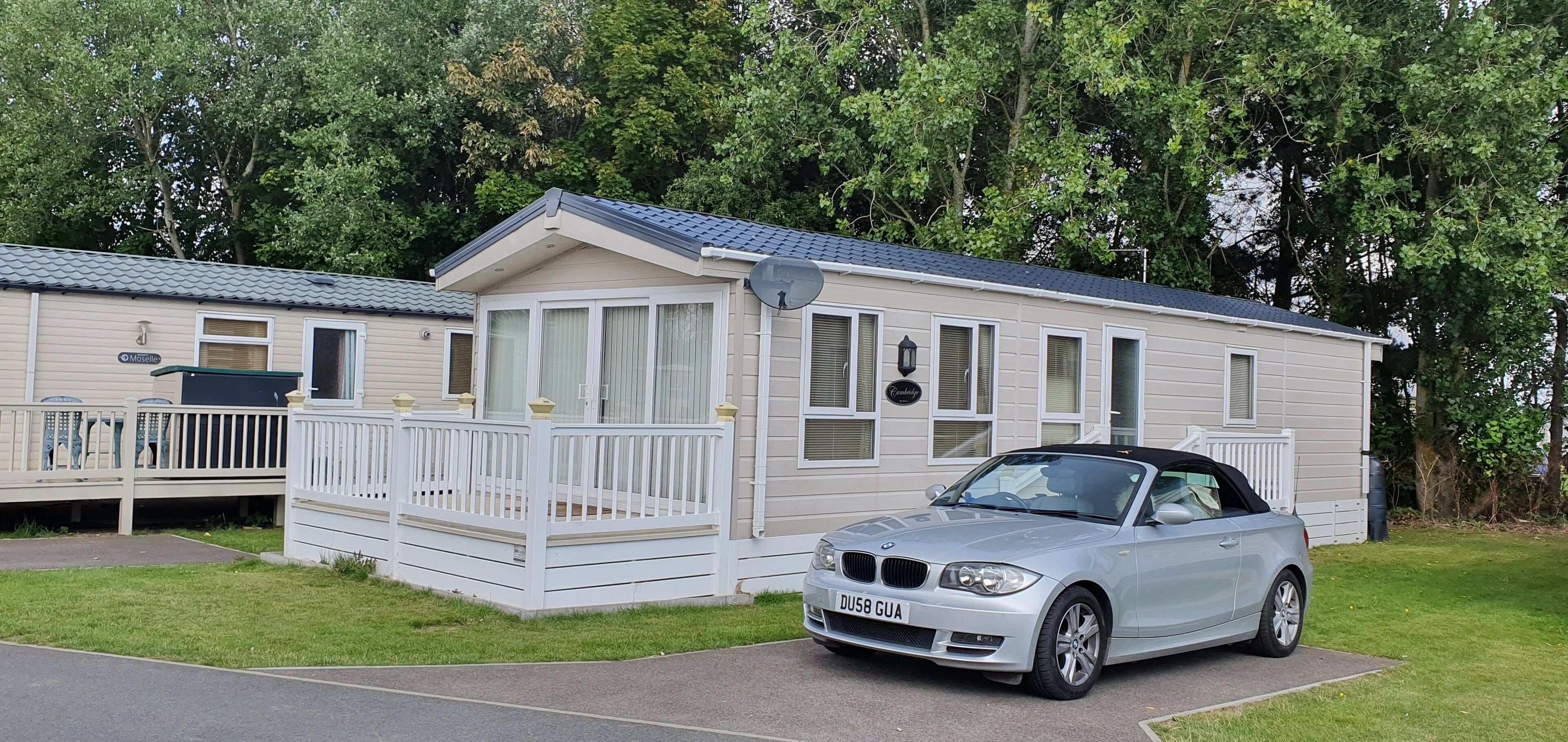 A mobile home with a white exterior and a balcony, parked in front of a wooded area.