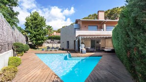 Ein Schwimmbad mit Holzterrasse, eine überdachte Terrasse und ein zweistöckiges Haus mit Balkon.