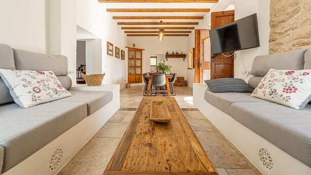 Uma sala de estar com dois sofás, uma mesa de centro de madeira e uma TV fixada na parede.