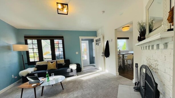 Een woonkamer met een bank, salontafel en open haard. Een deur leidt naar een andere kamer.