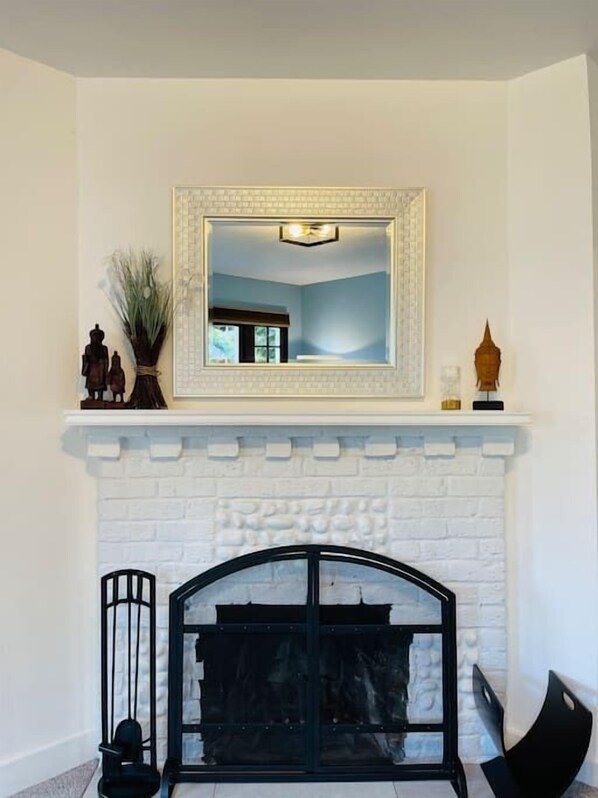 A room with a white brick fireplace, a black metal bench, and a mirror above the mantel.